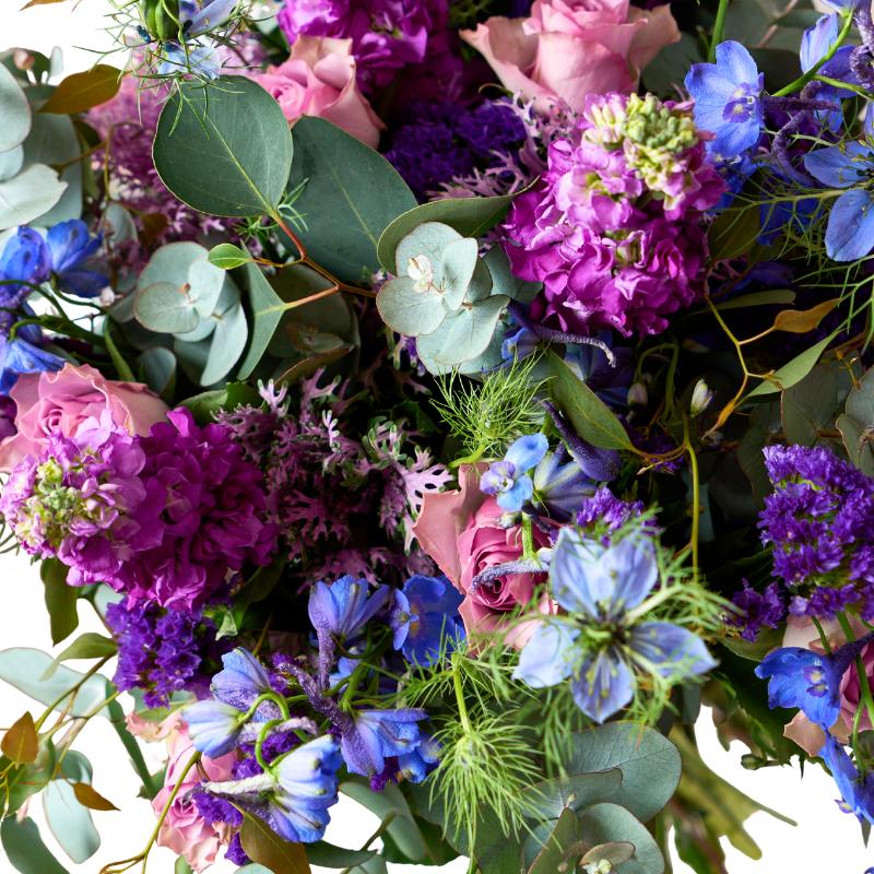 Bouquet of colorful flowers including purple, pink, and blue with green leaves.