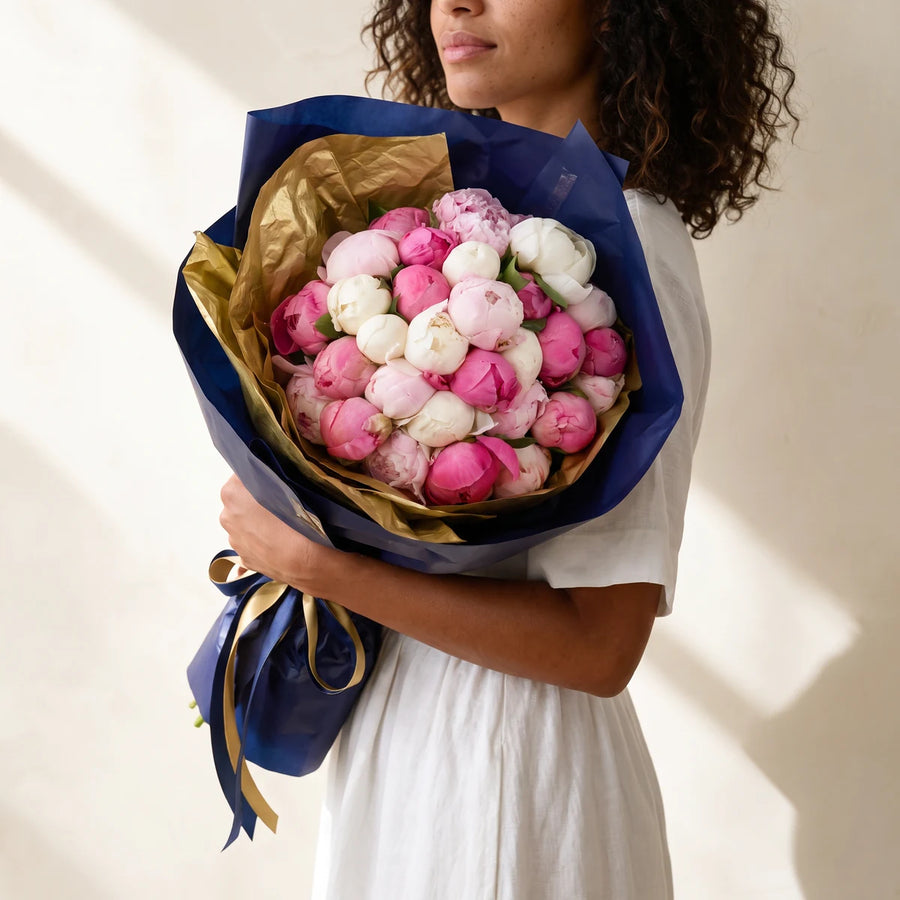Woman holding a luxury pink and white peony bouquet wrapped in gold and navy paper, same-day peony delivery Cape Town
