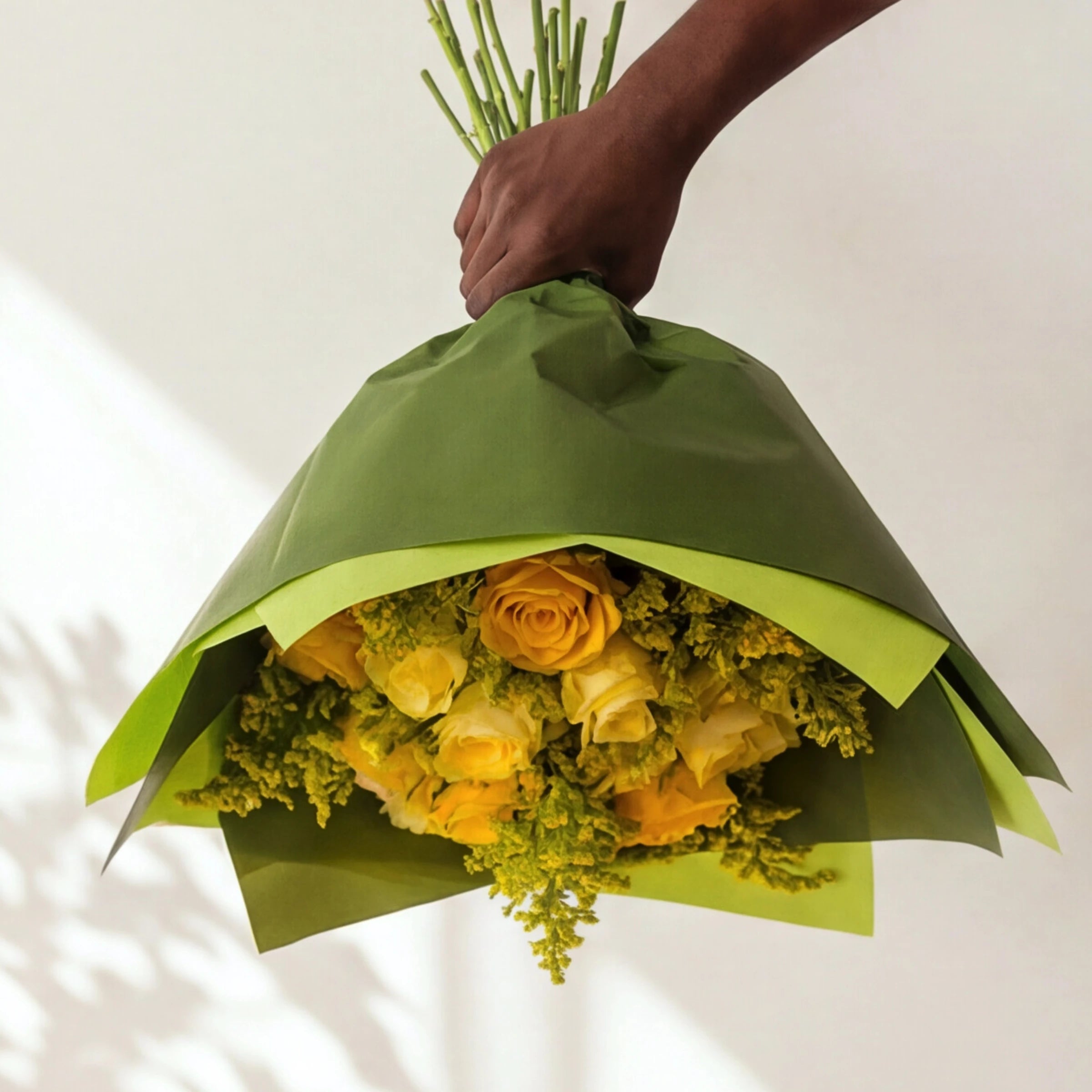 The Meadowlark bouquet held up, yellow roses and solidago peeking from green wrap