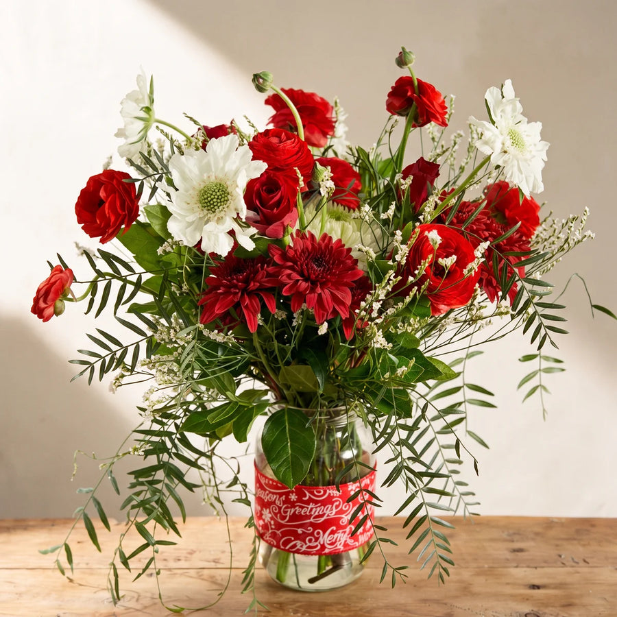 Red and white Christmas flowers in a glass jar with a red Season's Greetings band on a pine table, Fabulous Flowers South Africa
