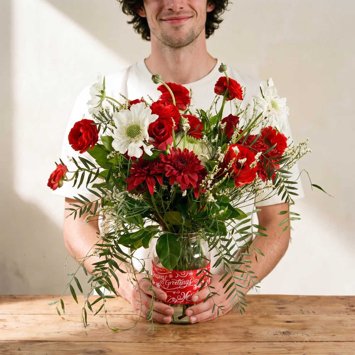 Man in a white t-shirt holding a jar of red and white Christmas flowers with trailing greenery, Fabulous Flowers South Africa