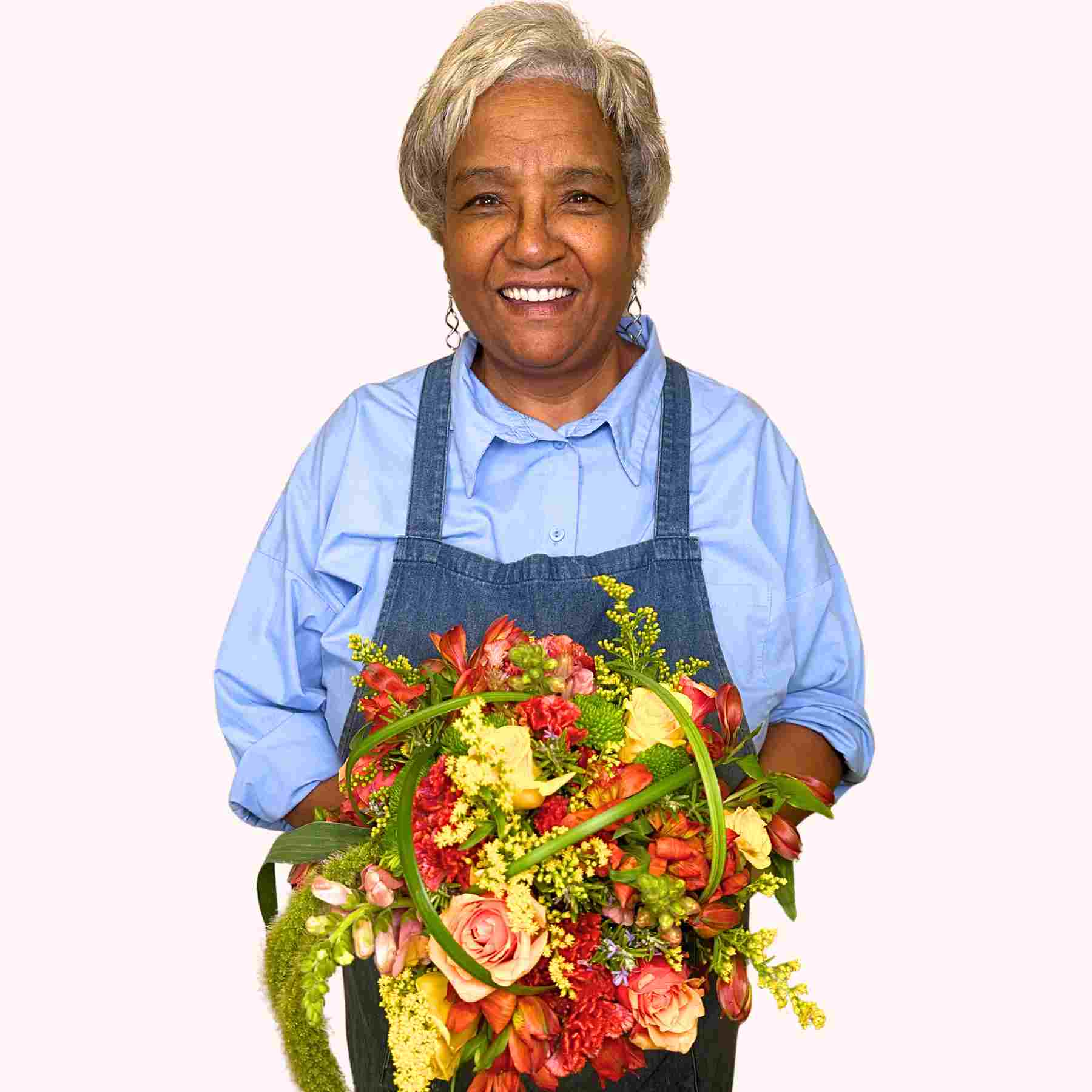 Cheerful florist with grey hair holding Moena's Flower Bouquet, featuring vibrant roses and lush foliage, from Fabulous Flowers and Gifts.