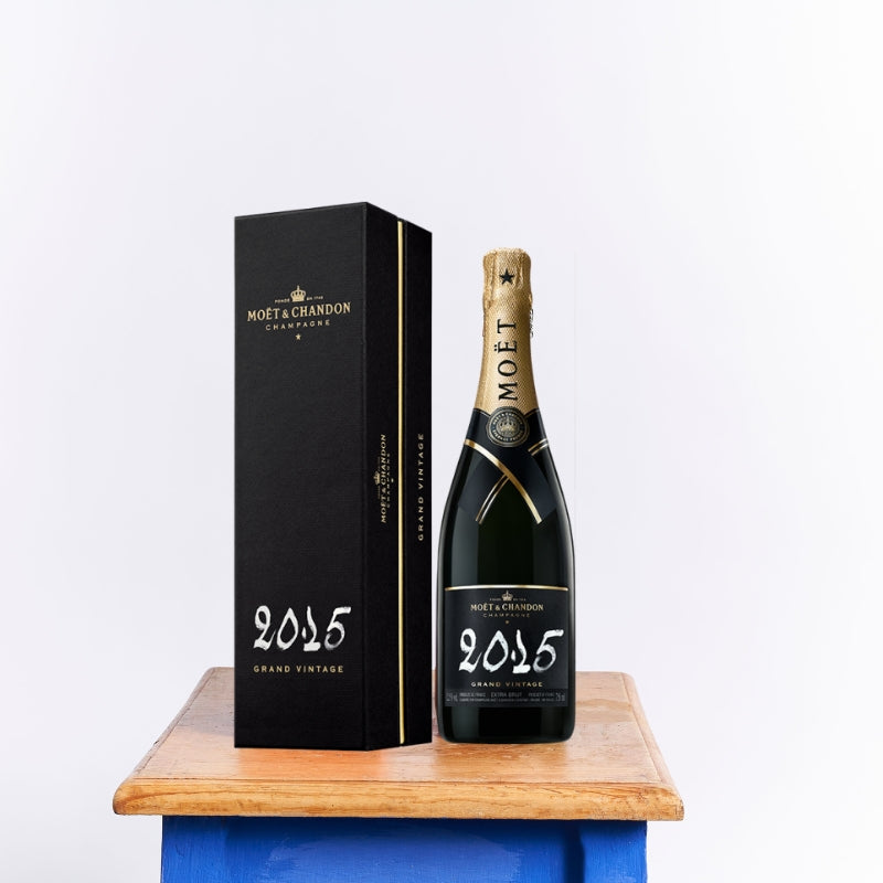 Moët & Chandon Grand Vintage 2015 champagne bottle with elegant black and gold packaging displayed on a wooden table.