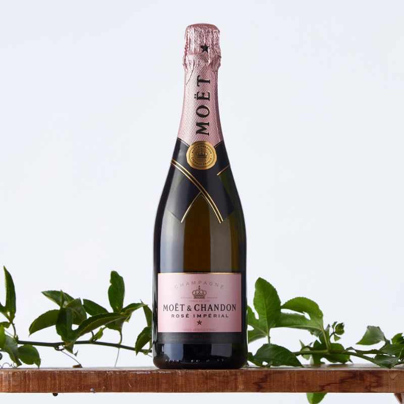 Bottle of Moët & Chandon Rosé Impérial champagne displayed on a wooden shelf with green foliage against a light background.