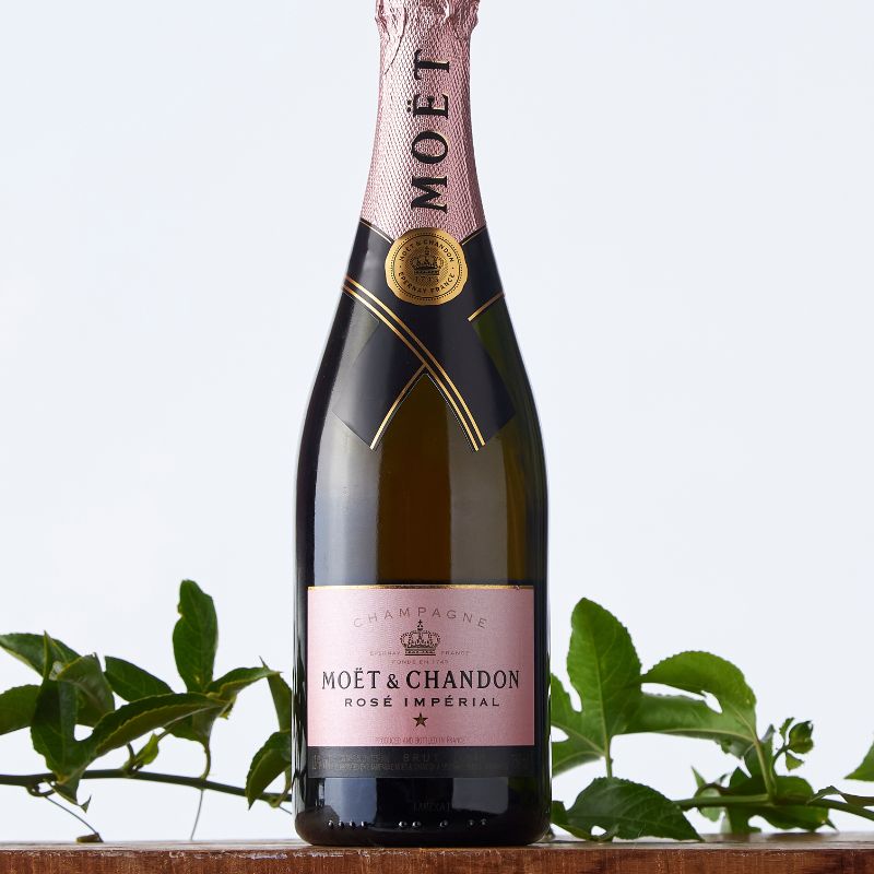 Close-up of Moët & Chandon Rosé Impérial champagne bottle with gold foil and pink label, surrounded by green leafy accents.