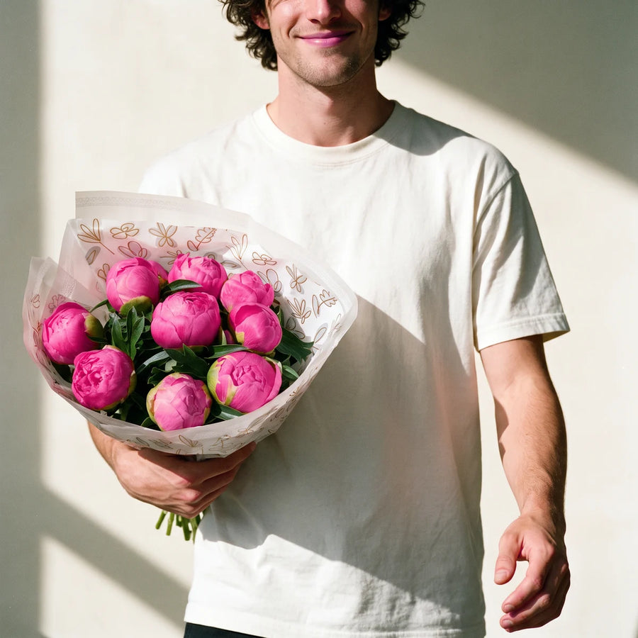 Smiling man with curly dark hair in a white t-shirt walking towards the camera carrying a large bouquet of twenty pink peonies, Fabulous Flowers South Africa