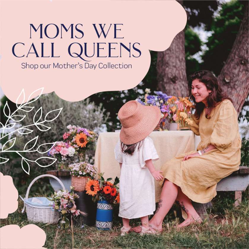 A serene outdoor setting with a mother in a golden dress smiling at her child in a white dress and sunhat, surrounded by vibrant Mother's Day Collection flowers, capturing the essence of 'Moms We Call Queens' at Fabulous Flowers and Gifts.