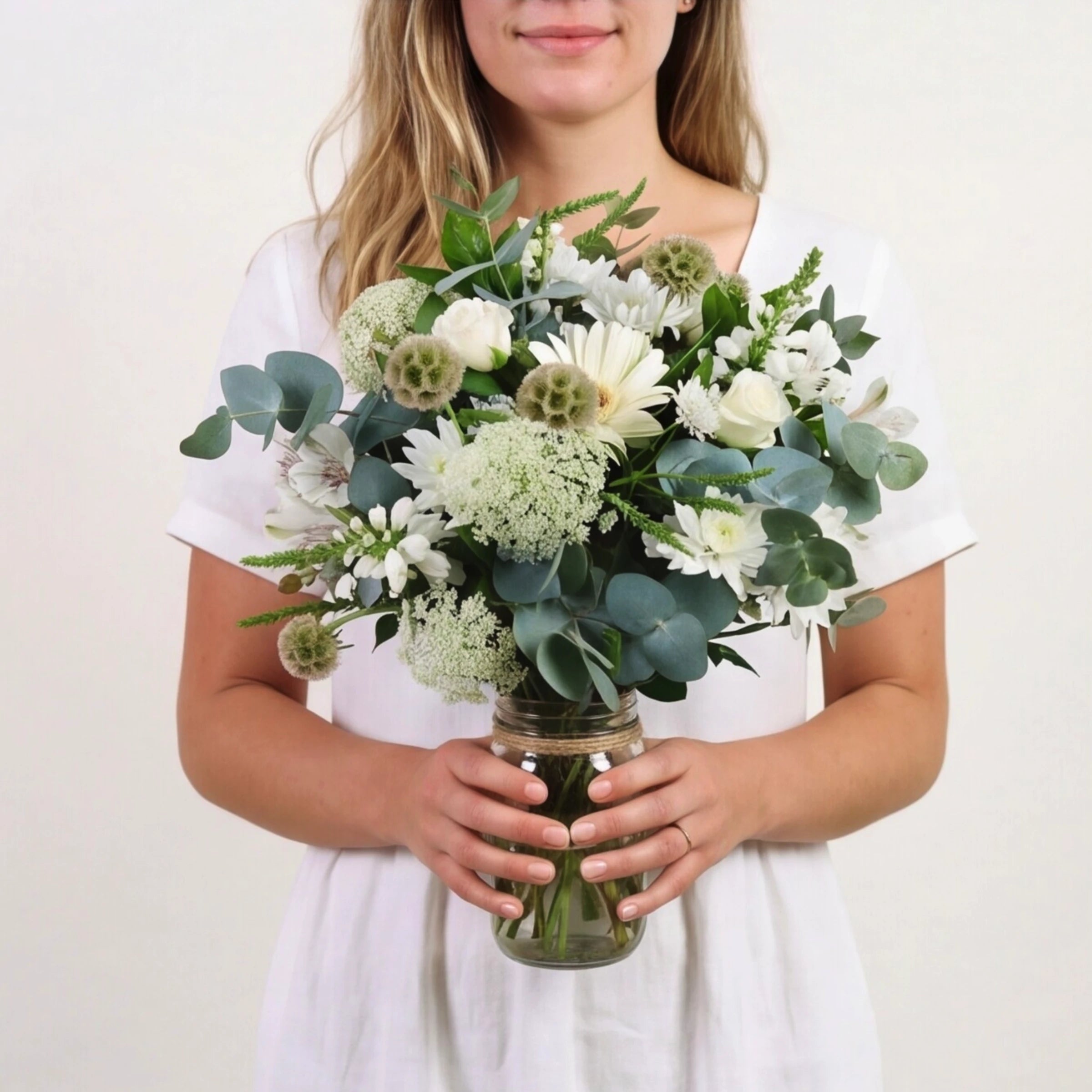 Woman in white holding Peace in a Jar from Fabulous Flowers South Africa, white roses, white gerbera, chrysanthemums, scabiosa pods, Queen Anne's lace and eucalyptus in a twine-tied glass jar for sympathy and same-day Cape Town and Johannesburg delivery