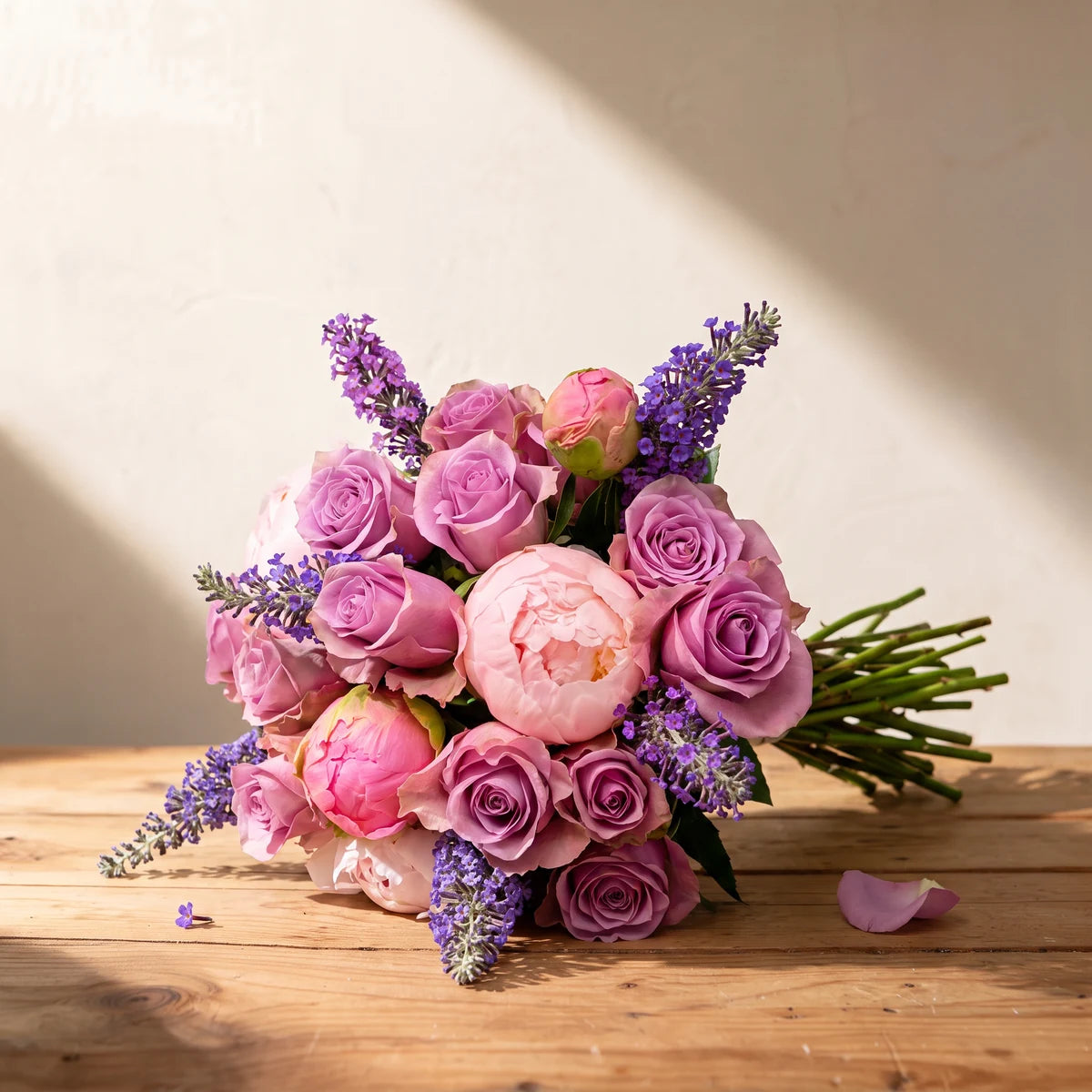 Bouquet of blush pink peonies, lilac roses and purple lavender lying on a wooden table in afternoon sun