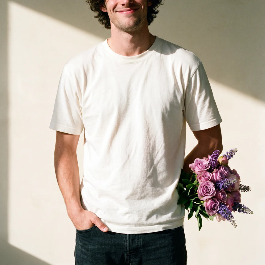 Smiling man in a white T-shirt holding a bouquet of lilac roses behind his back