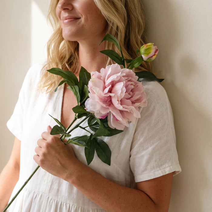Woman holding a single mauve silk peony stem over her shoulder