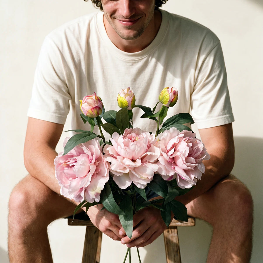 Man seated holding three mauve peony artificial flowers, a long-lasting gift