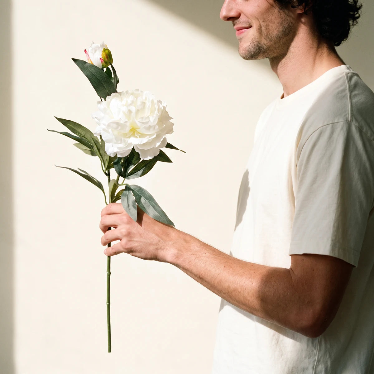 Man holding a white peony artificial flower in window light