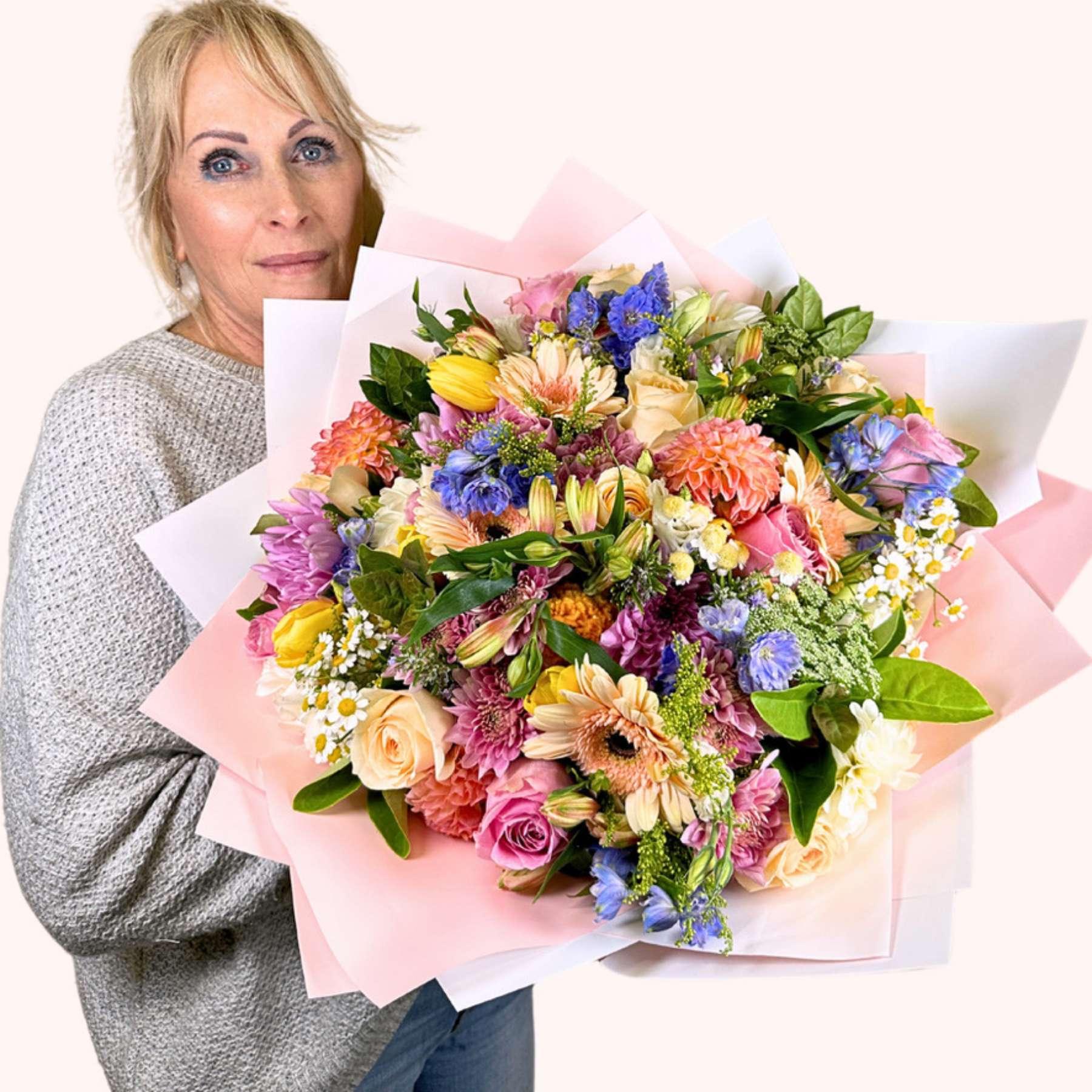 A woman with bright eyes smiling as she holds the Pink Passion Flower Bouquet, an abundant arrangement of pink, blue, yellow, and cream flowers, symbolizing a vibrant celebration of life and colour, available at Fabulous Flowers and Gifts.