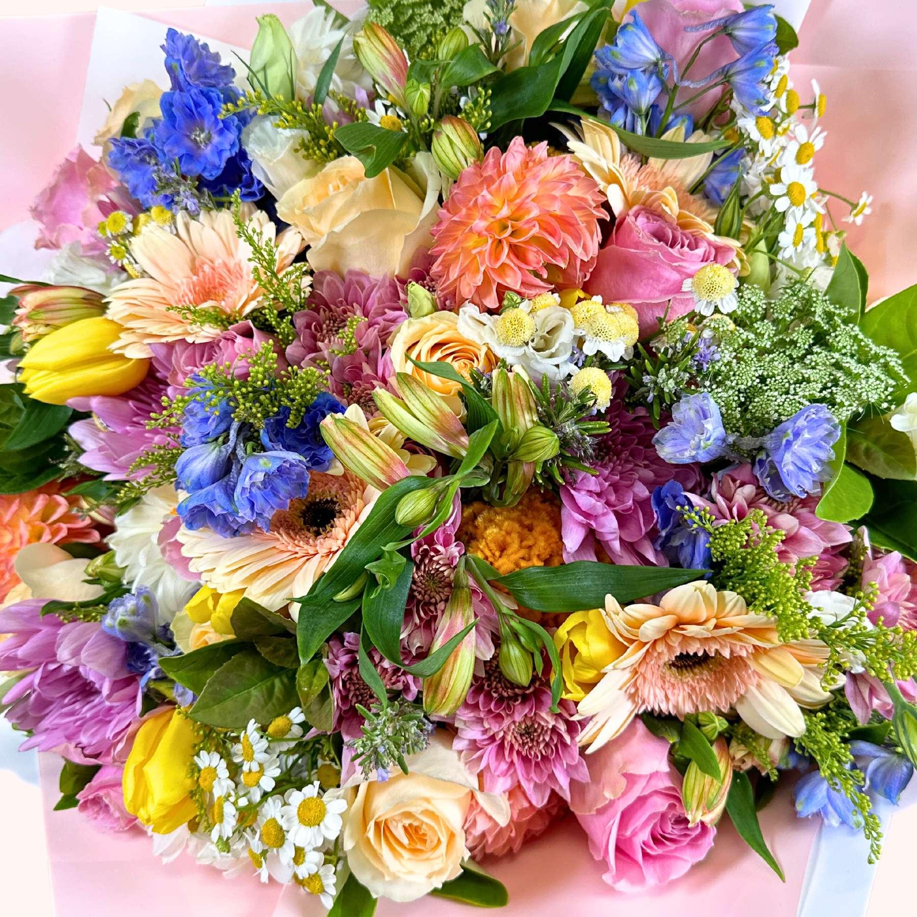 A woman with bright eyes smiling as she holds the Pink Passion Flower Bouquet, an abundant arrangement of pink, blue, yellow, and cream flowers, symbolizing a vibrant celebration of life and colour, available at Fabulous Flowers and Gifts.
