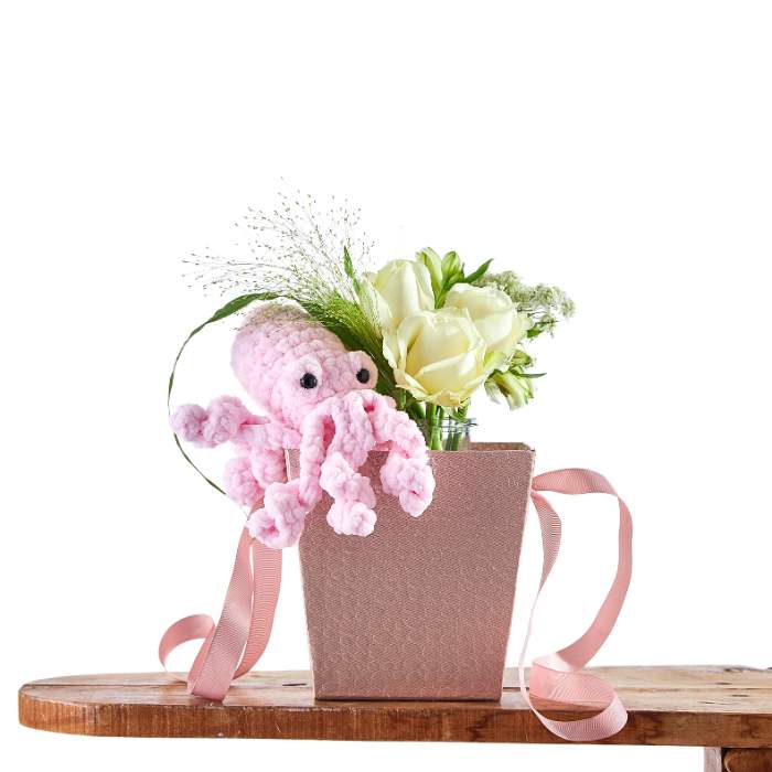 Pink octopus toy in a decorative box with flowers on a white background