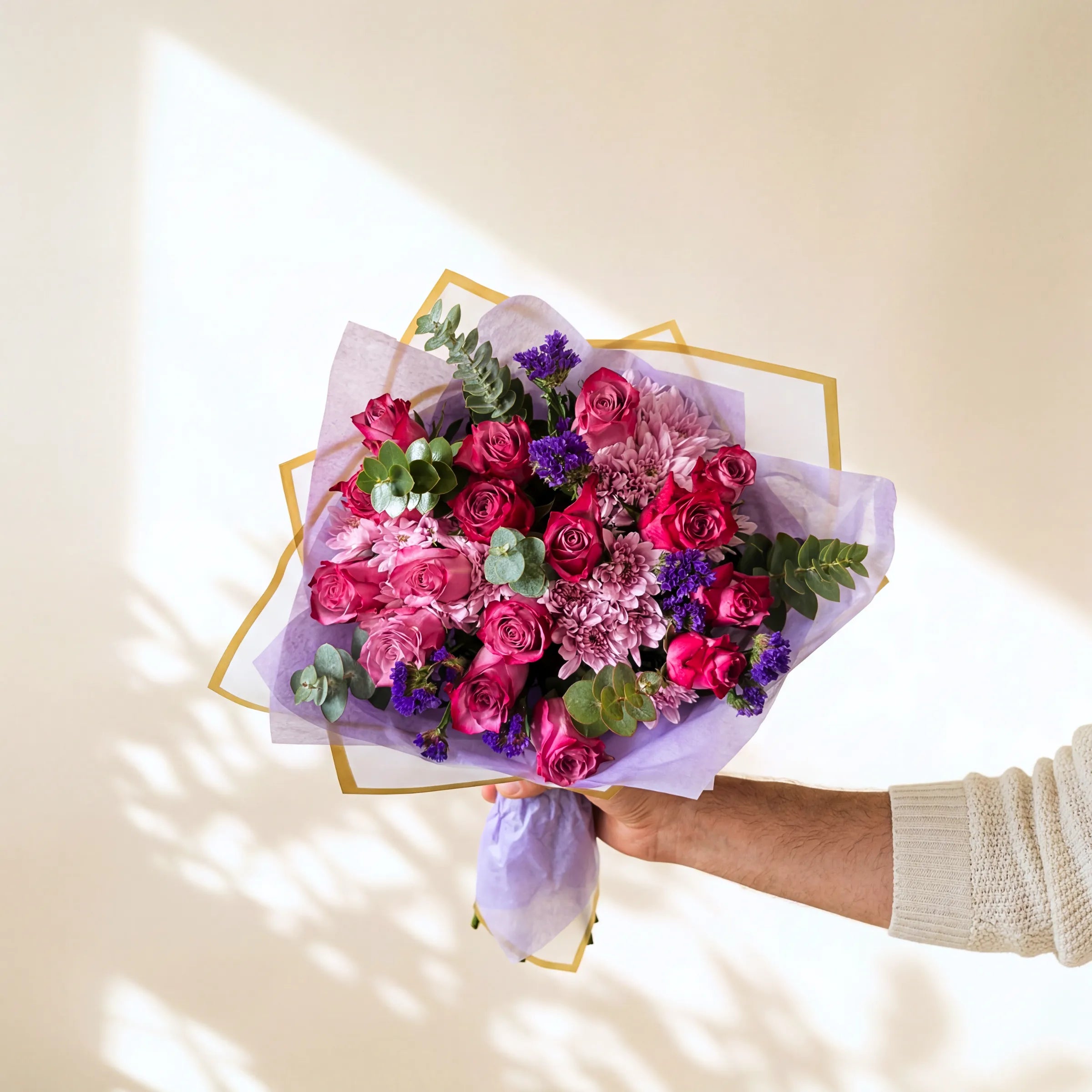 Bouquet of pink and purple flowers held by a person against a light background