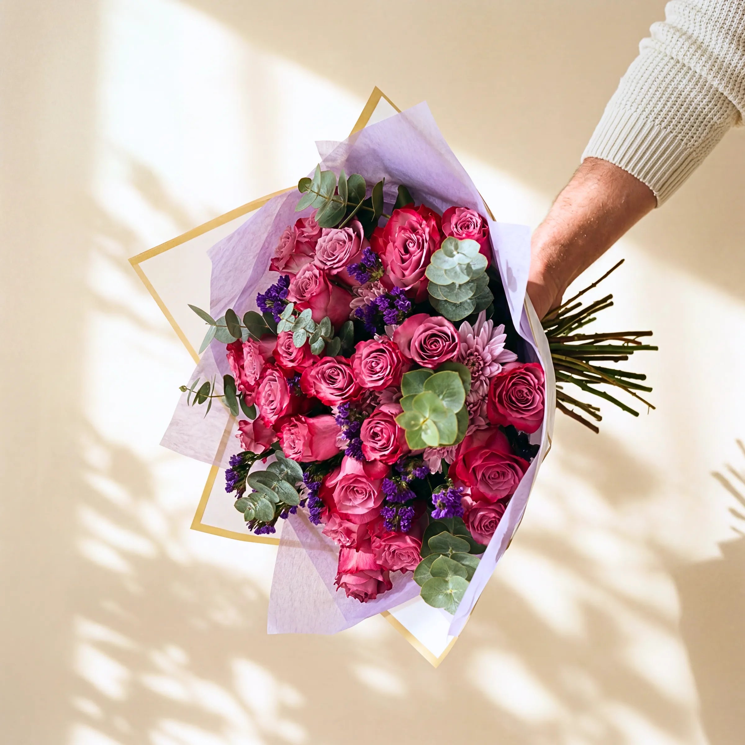 Bouquet of pink roses and greenery held by a person against a light background