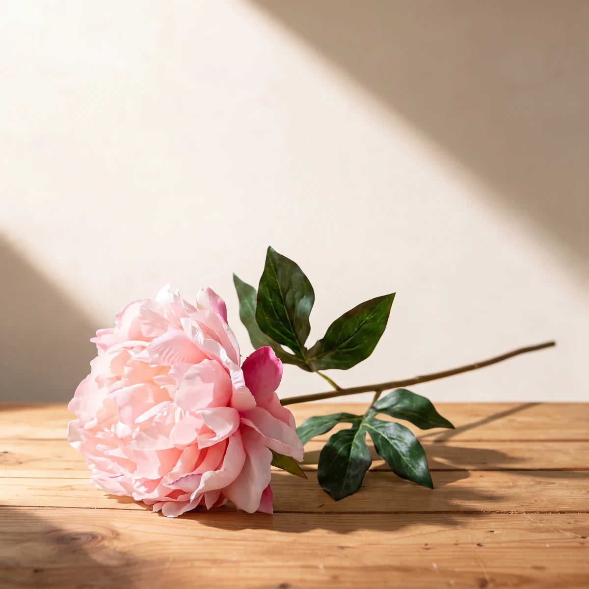 Pink peony artificial flower, a single silk stem lying on a wooden table
