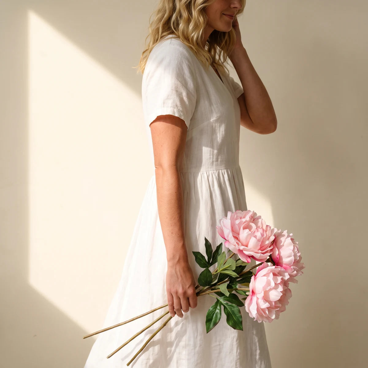 Woman carrying three pink silk peony stems, a long-lasting flower gift