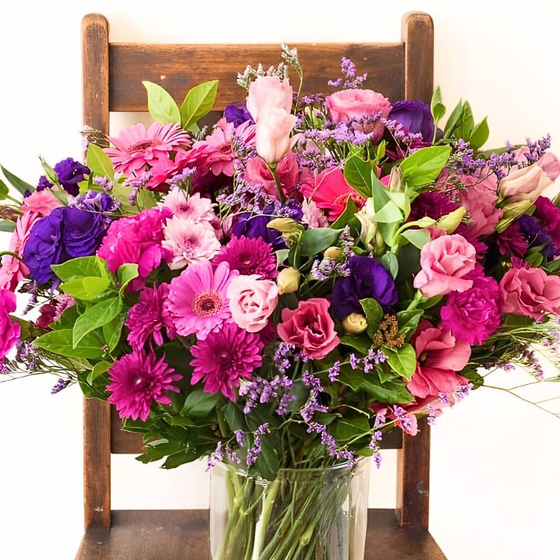 Big arrangement of colourful in a clear vase on a wooden chair.