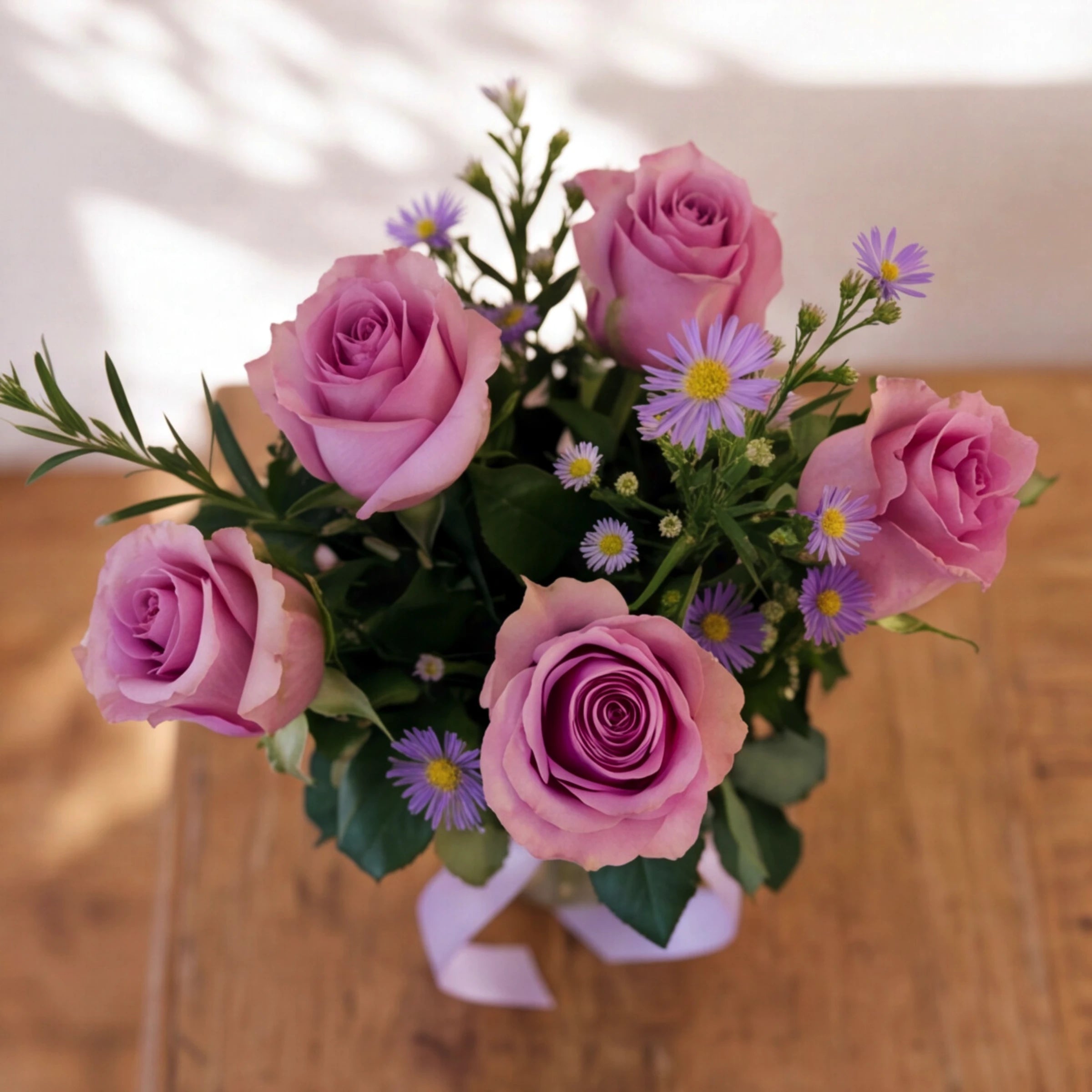 Overhead view of the Provence lavender rose arrangement, five soft lilac roses ringed with purple asters and foliage