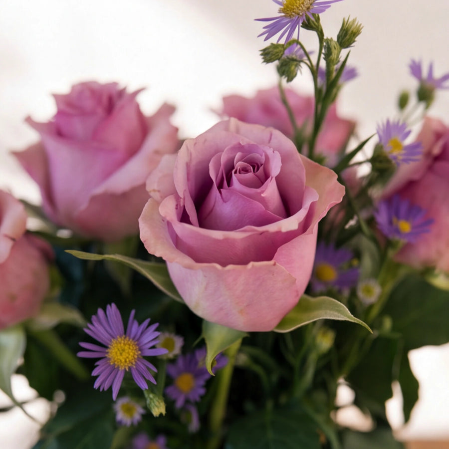 Close-up of a single lavender rose beside delicate purple asters in the Provence arrangement by Fabulous Flowers