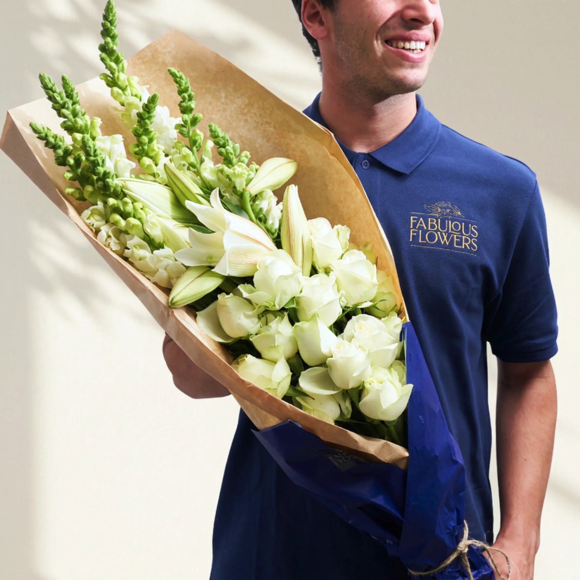 Fabulous Flowers courier holding the Elegant White Bouquet of white roses, lilies and snapdragons in kraft wrap