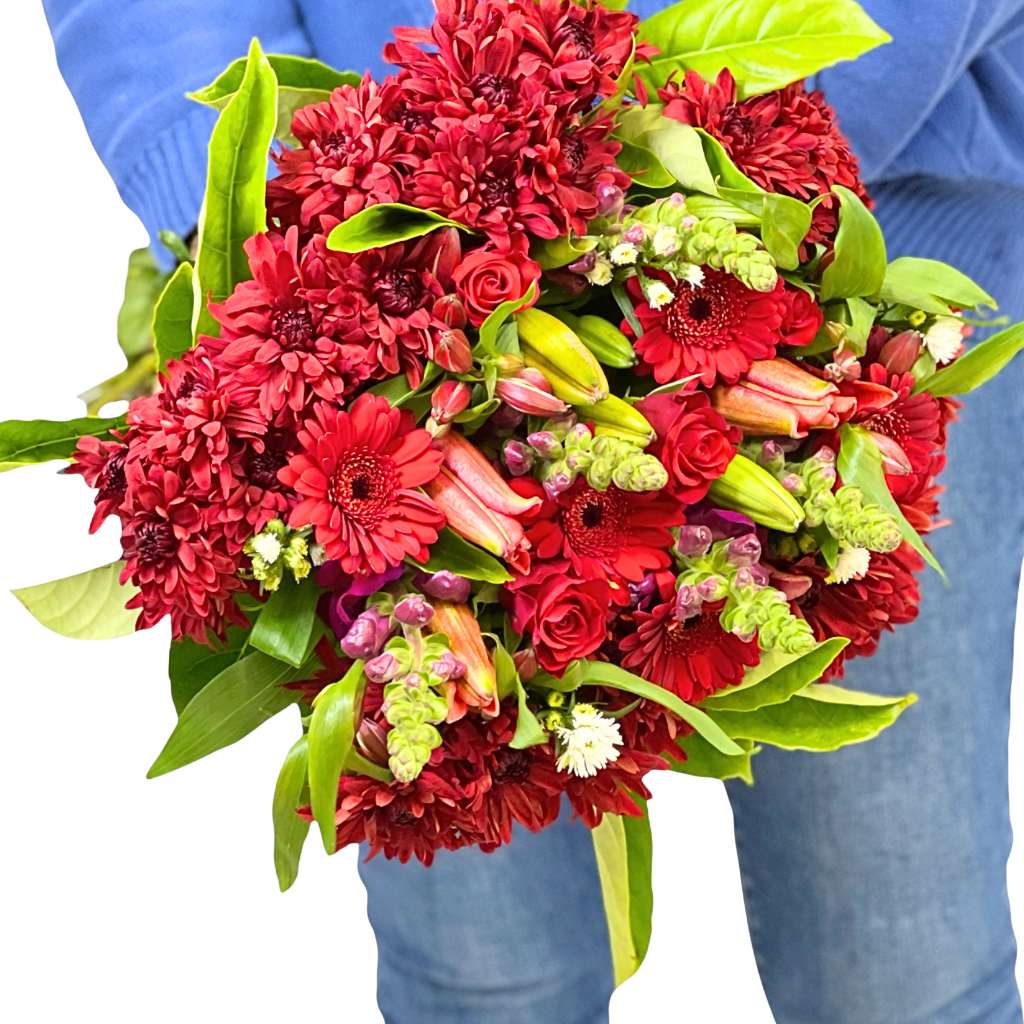 Bouquet of red and green flowers held by a person wearing blue jeans.