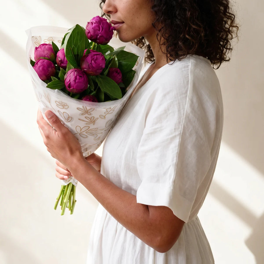 Woman with curly dark hair in a white dress, seen in profile, smelling a bouquet of magenta Red Sarah Bernhardt peonies, Fabulous Flowers South Africa