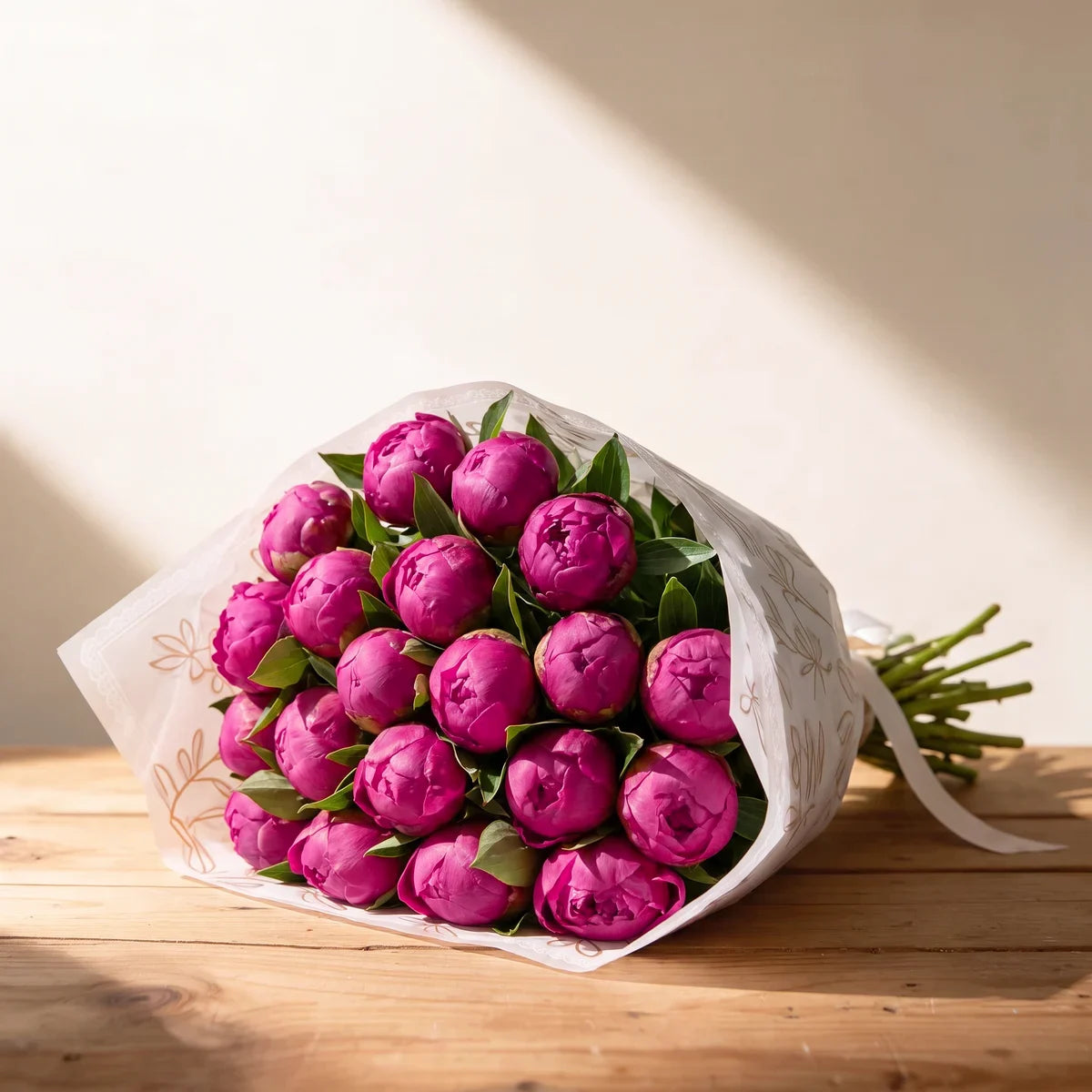 Twenty Red Sarah Bernhardt peonies in deep magenta bud, wrapped in white paper with a gold leaf print on a pine table in afternoon sunlight, Fabulous Flowers South Africa