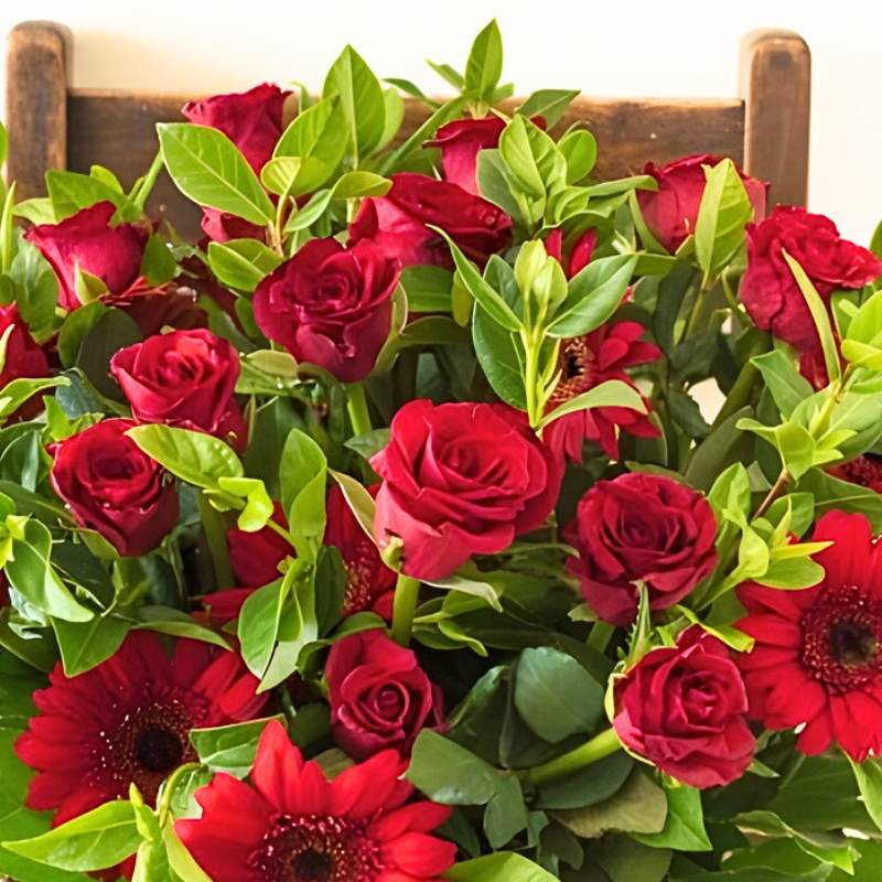 Large arrangement of red roses and green leaves on a wooden surface