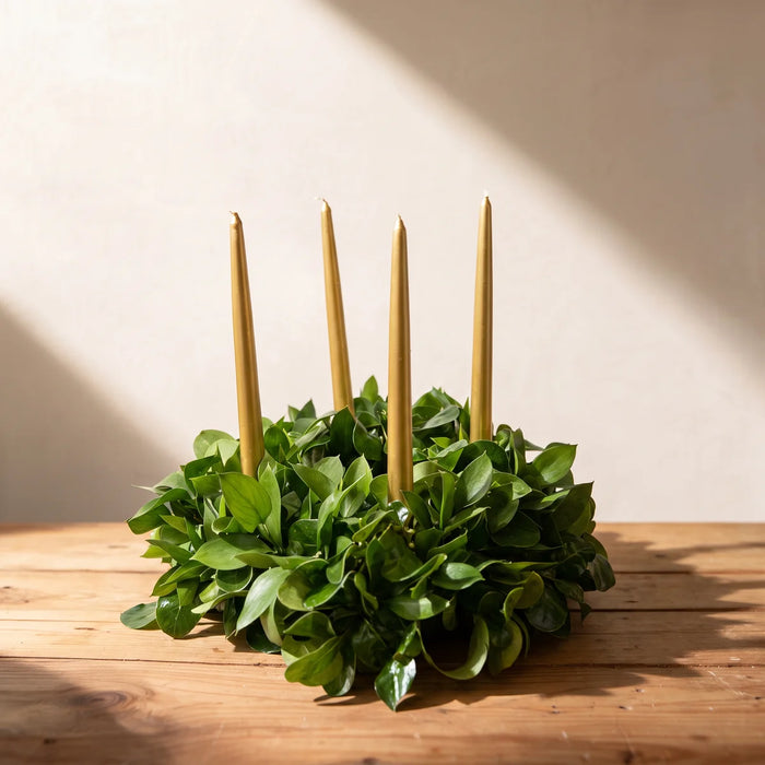 Round table wreath of fresh glossy green leaves with four gold taper candles on a pine table, Fabulous Flowers South Africa
