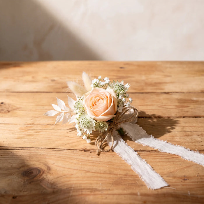 Wrist corsage of a peach rose, white astrantia, gypsophila and bunny tails with frayed linen ribbon on a wooden table, Fabulous Flowers South Africa
