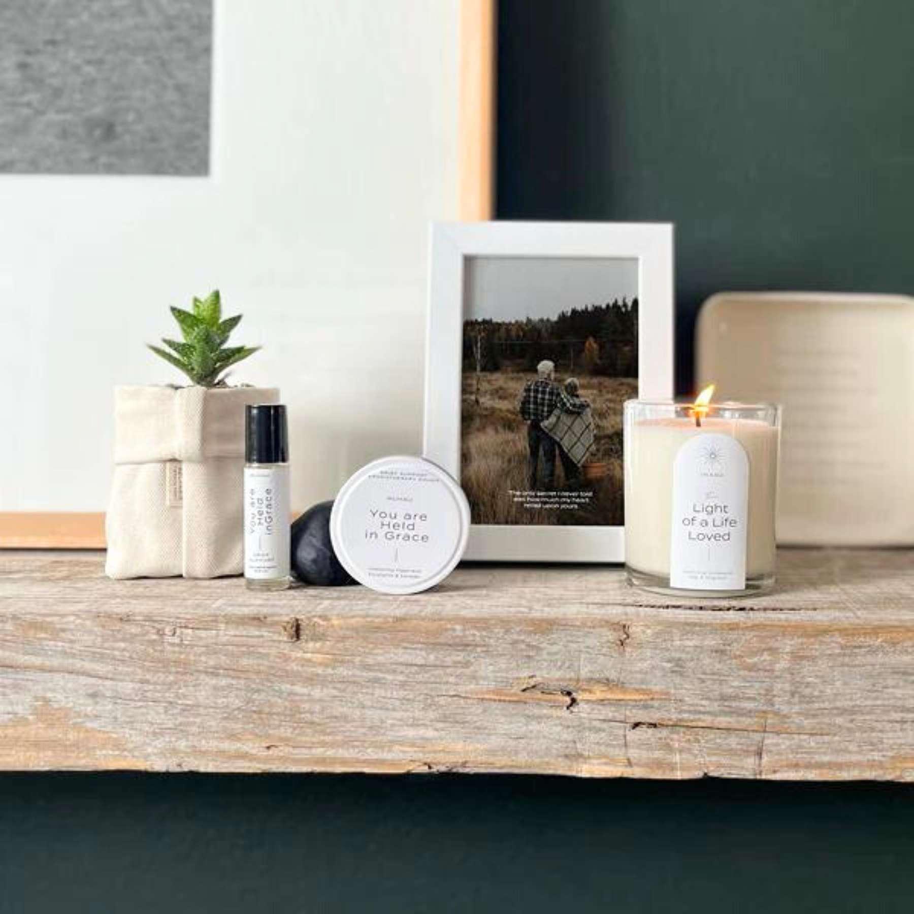 A serene display featuring a SOLANDIS plant in a fabric pot, wellness products, a framed photograph, and a lit candle, arranged on a wooden surface for a touch of tranquillity from Fabulous Flowers and Gifts.