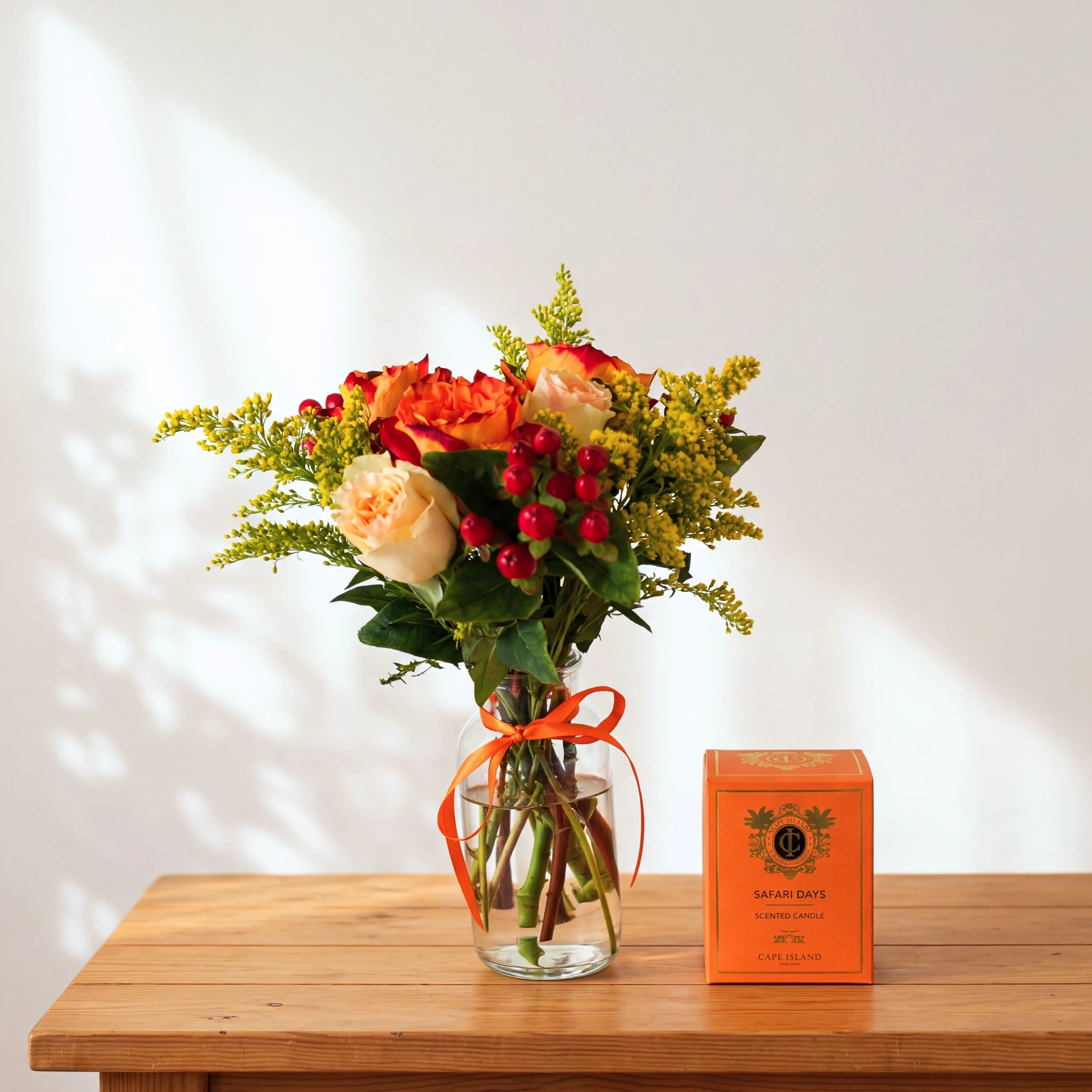 Savanna & Sun gift set with orange and cream roses in a vase beside a Cape Island Safari Days scented candle box