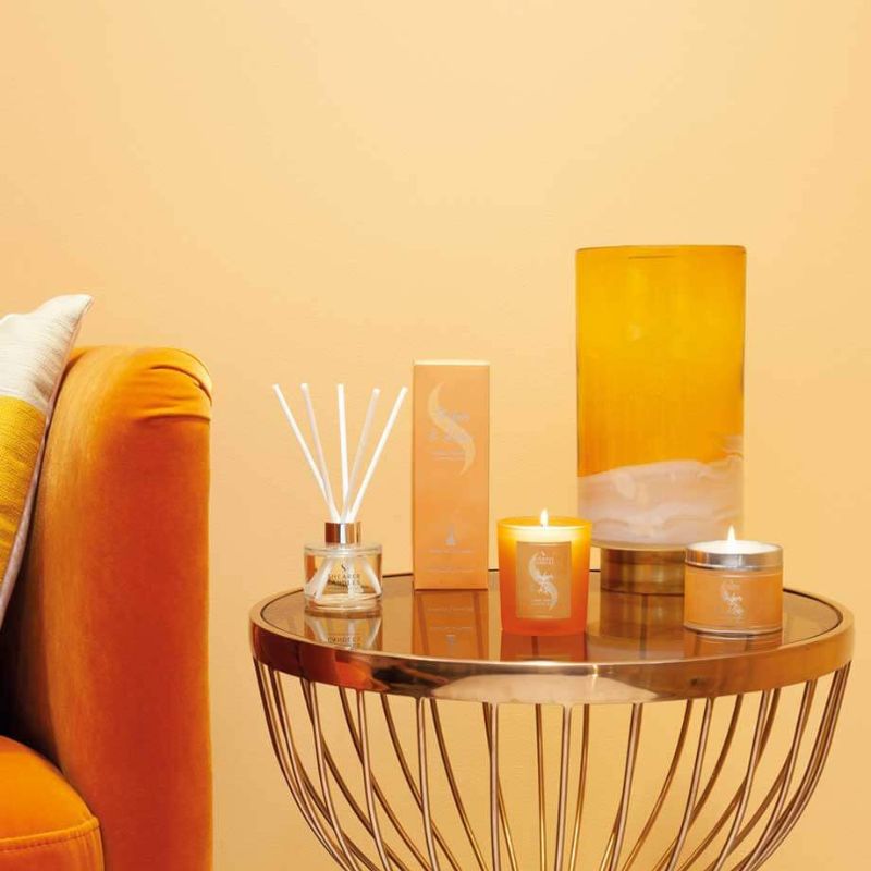 Decorative items including candles and a diffuser on a table against an orange wall.