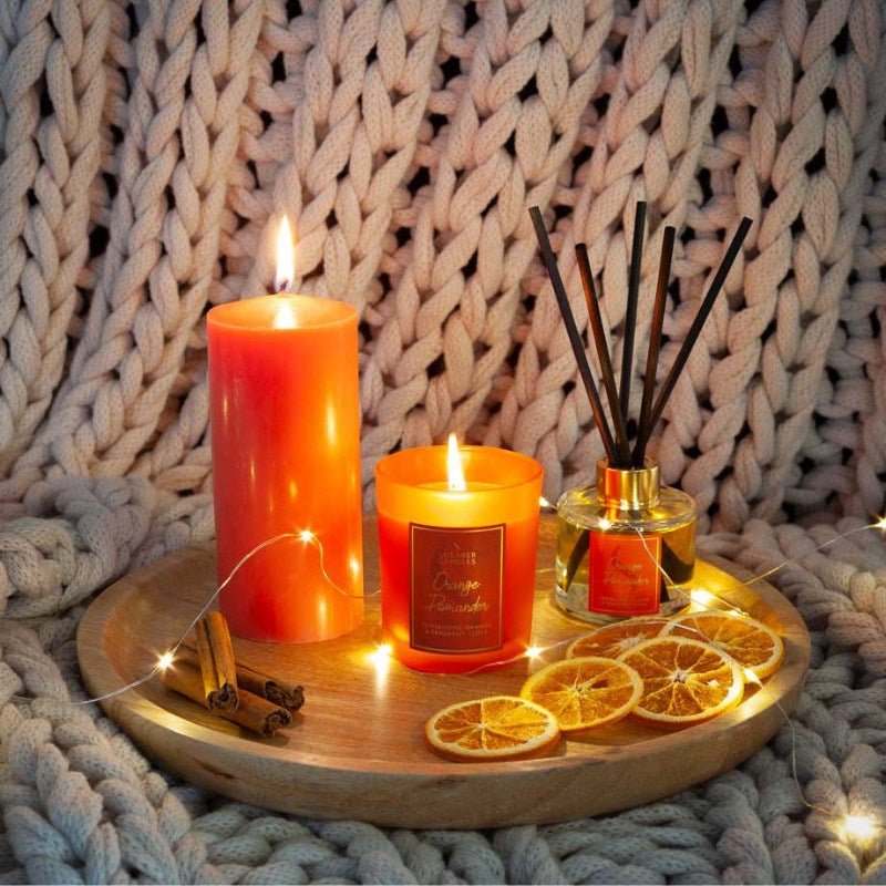 Candle, diffuser, and dried oranges on a wooden tray with a knitted background