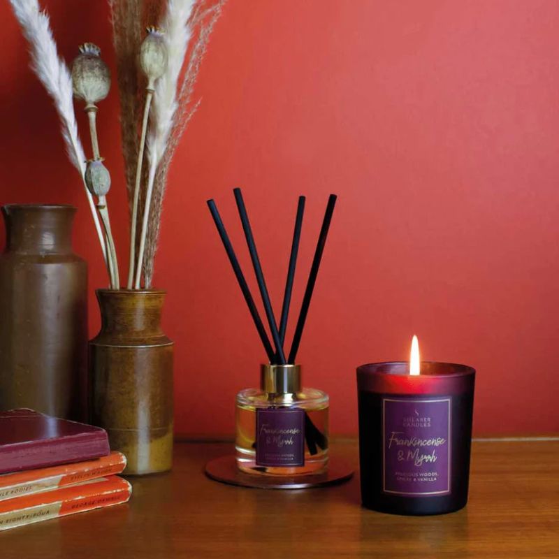 Candle and diffuser with decorative elements on a wooden surface against a red wall