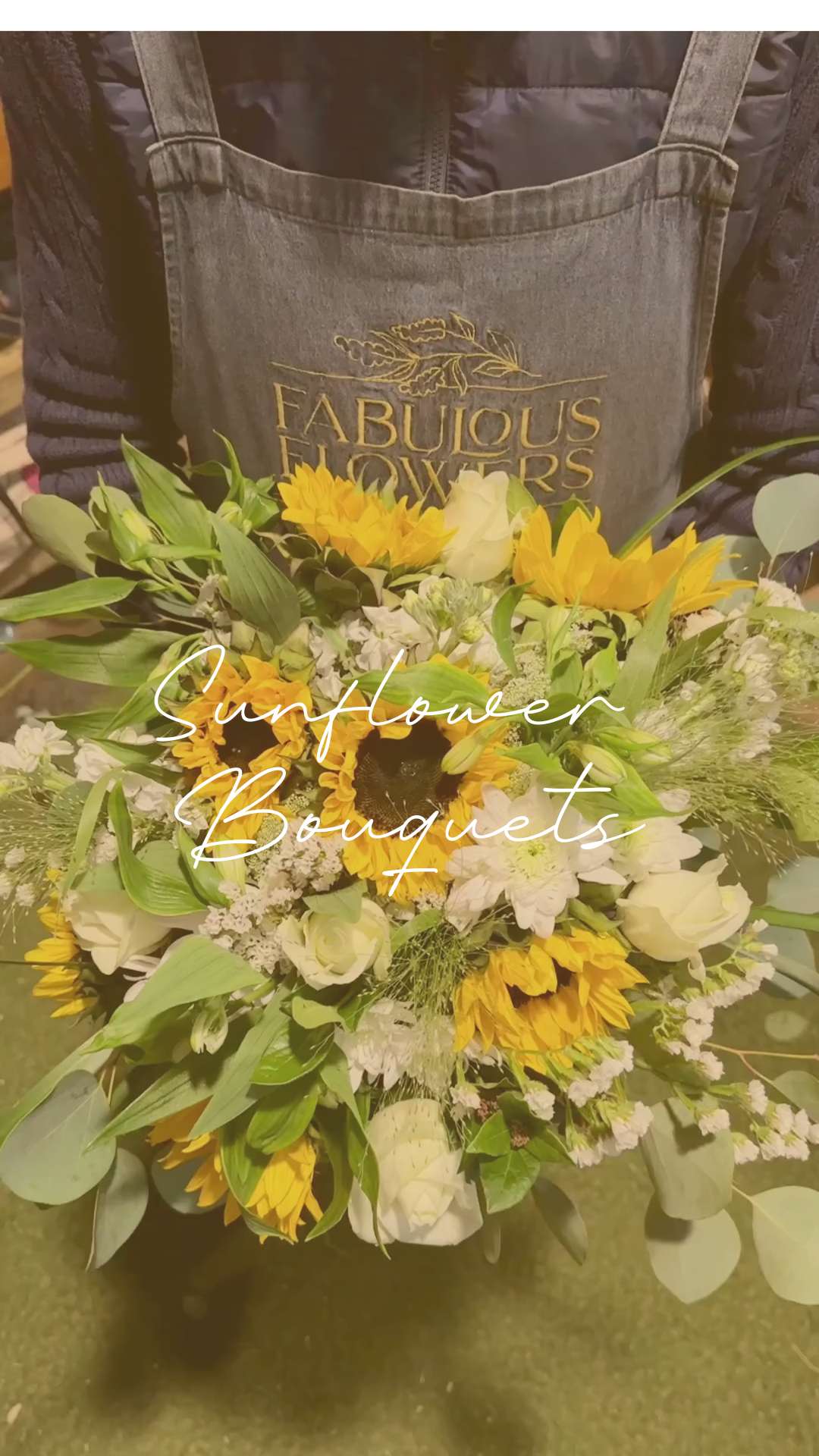 Person wearing a Fabulous Flowers apron holding a bouquet of sunflowers and white roses, with the text 'Sunflower Bouquets' overlayed on the image.