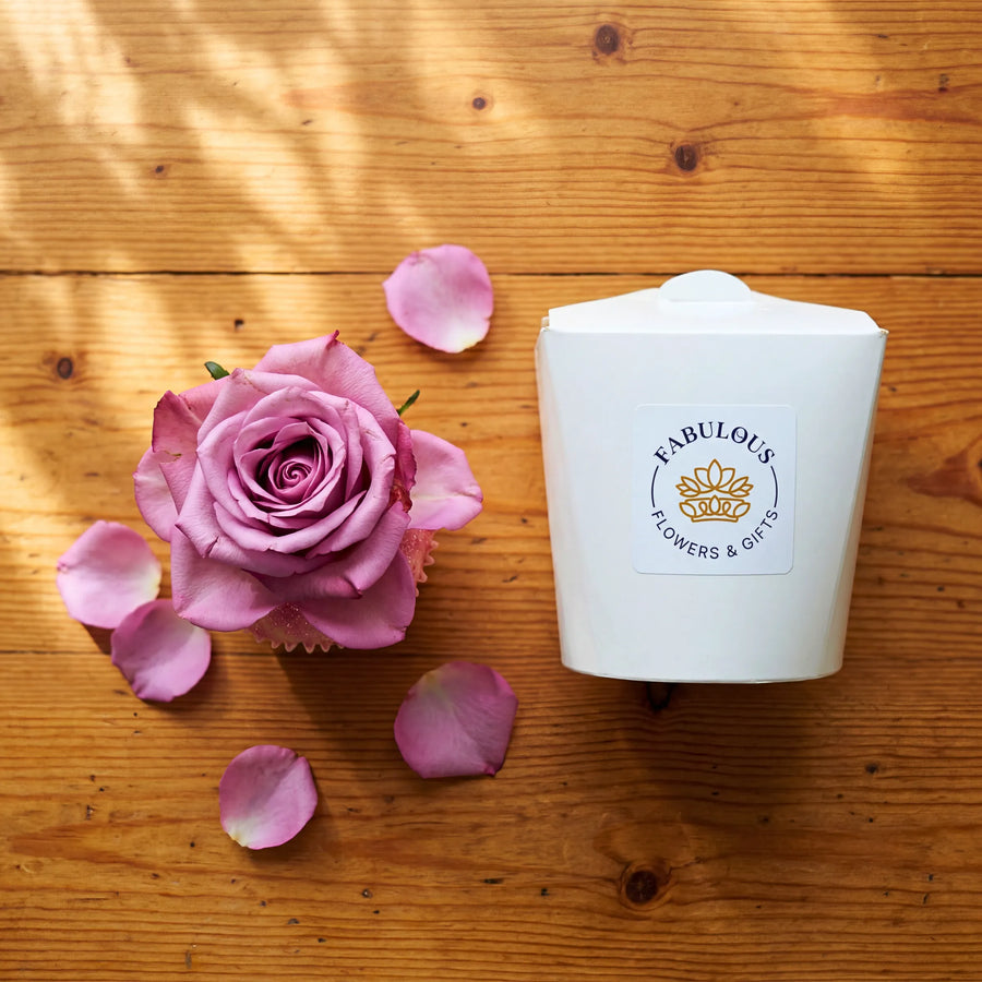 Single Vanilla Cupcake with pink rose, scattered rose petals and Fabulous Flowers gift box on wooden table