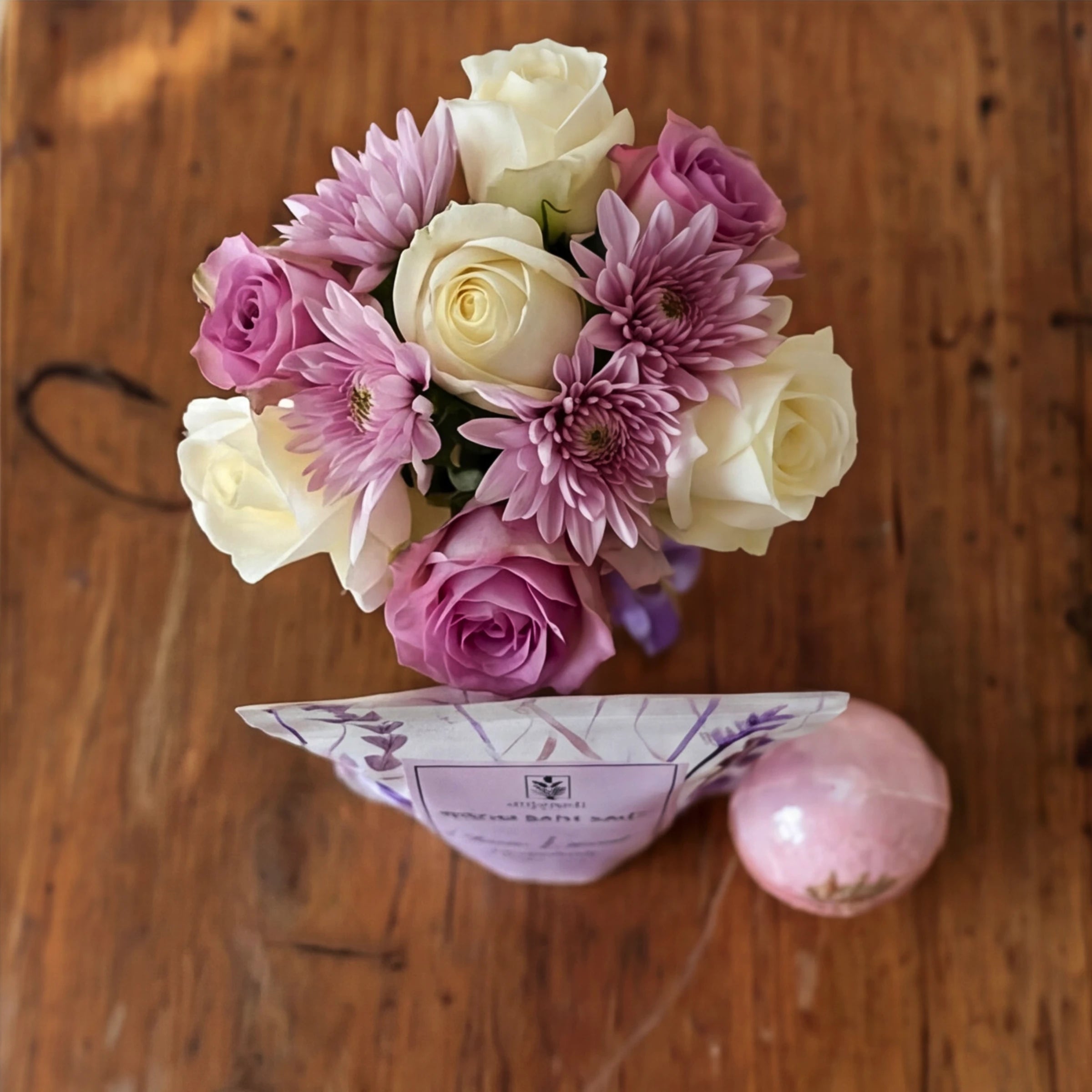 Top-down view of the Soak & Soothe posy of pink, lilac and cream roses with bath salts and a rose bath bomb