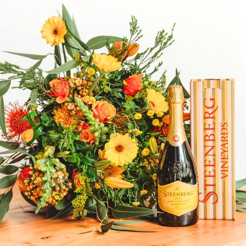 Sparkling Orange Bouquet with orange and yellow blooms beside a sparkling wine bottle and gift box on a wooden surface