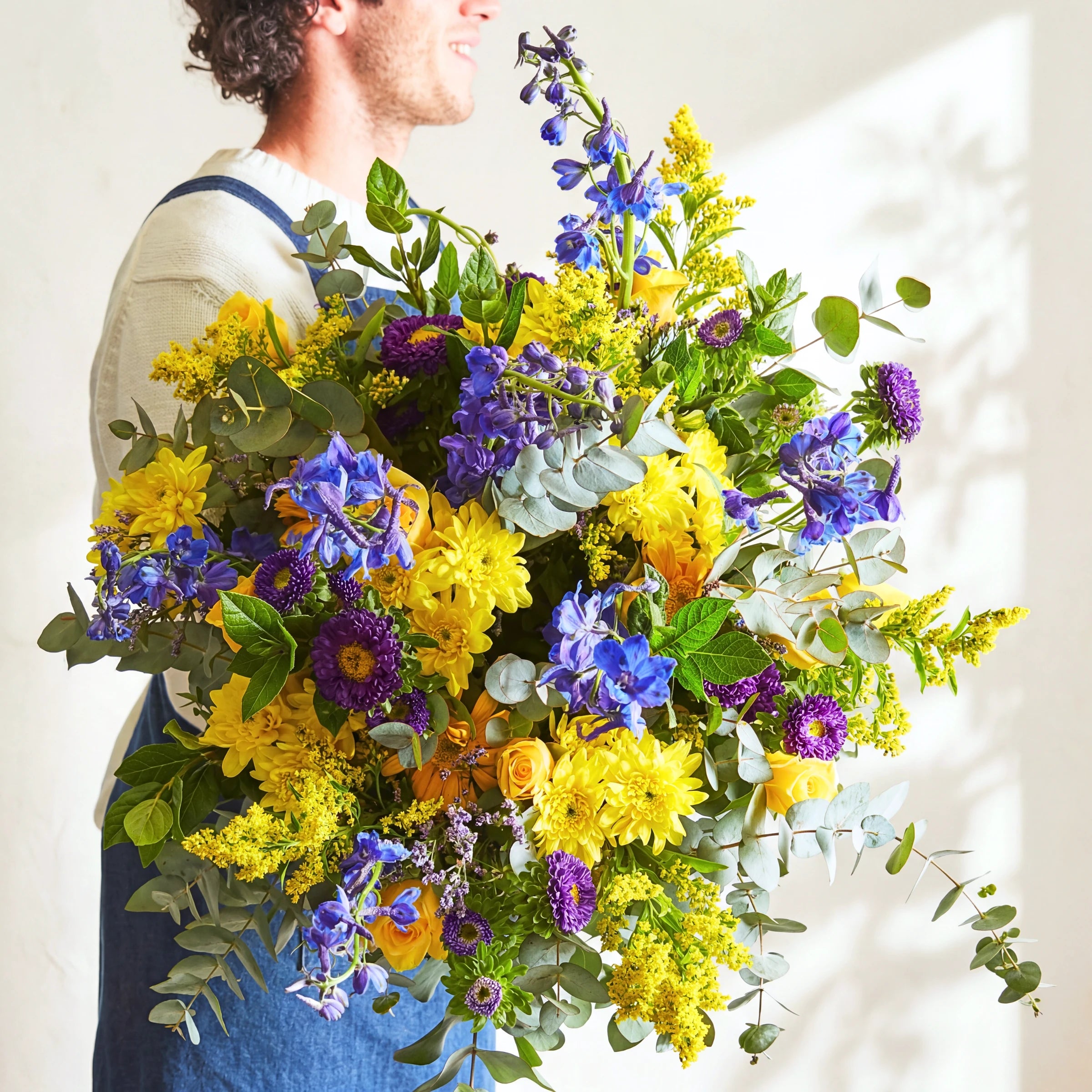 Florist holding the Spring Personified spring bouquet of blue delphinium, yellow chrysanthemums and purple asters.