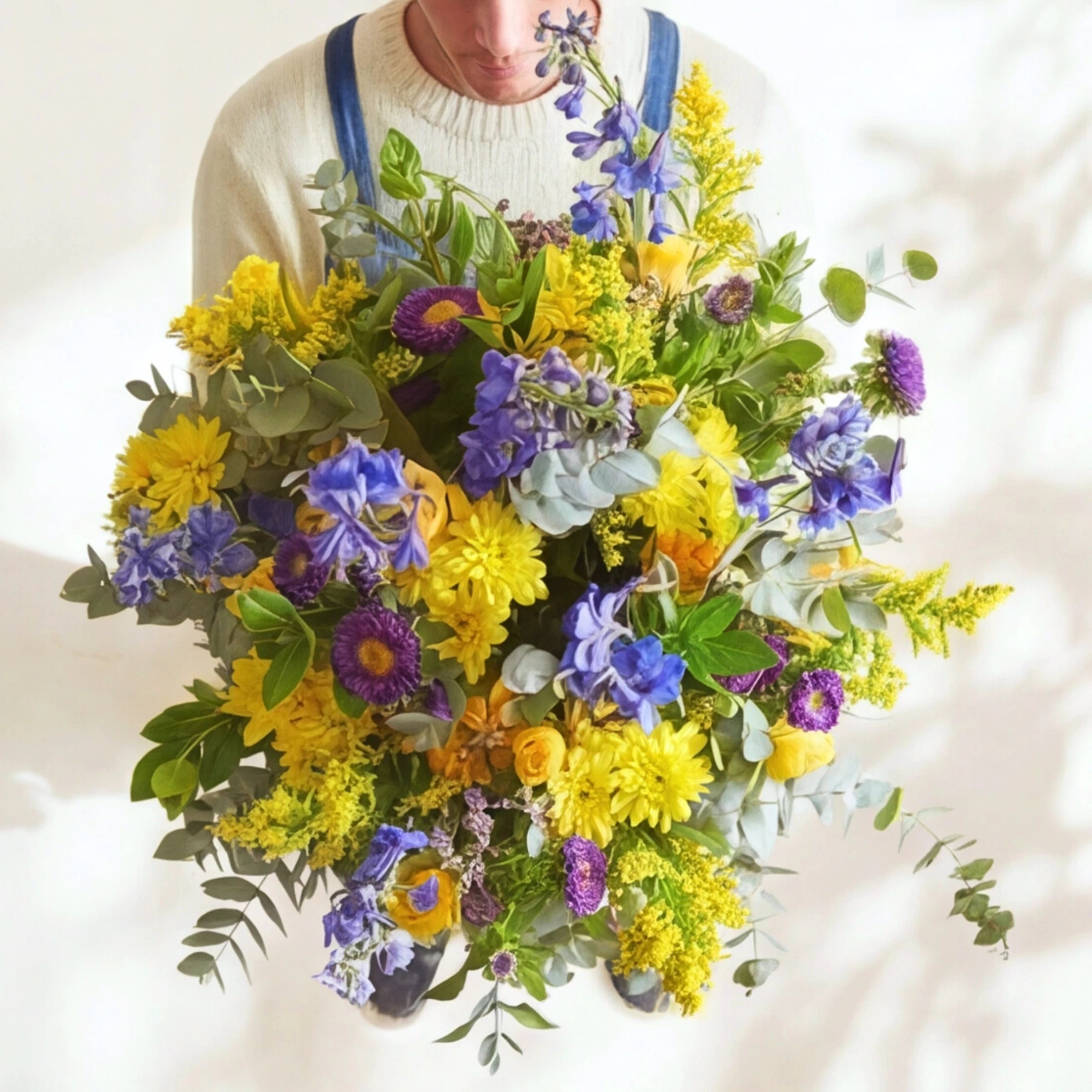 Spring Personified bouquet held close, yellow chrysanthemums, blue delphinium, purple asters and eucalyptus.