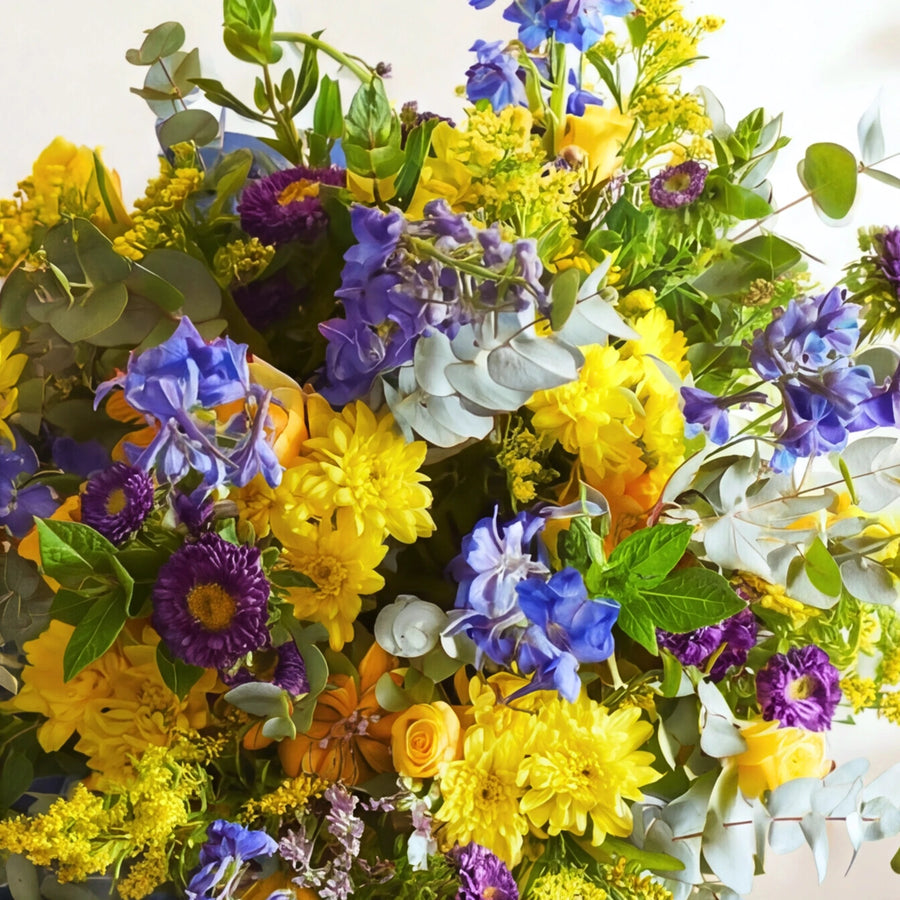 Close-up of the spring bouquet: yellow chrysanthemums, purple asters, blue delphinium, goldenrod and eucalyptus.