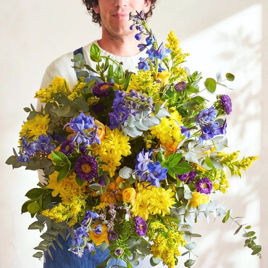 Florist smelling a blue delphinium stem in the Spring Personified spring bouquet with yellow chrysanthemums.