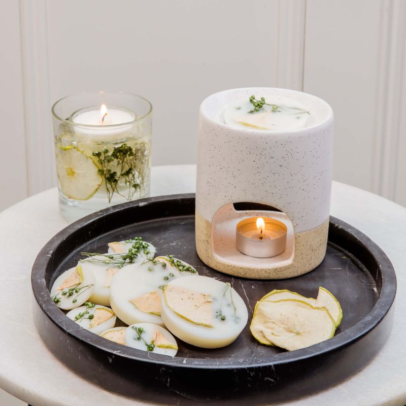 Ceramic diffuser with a candle on a tray with sliced pears and herbs.