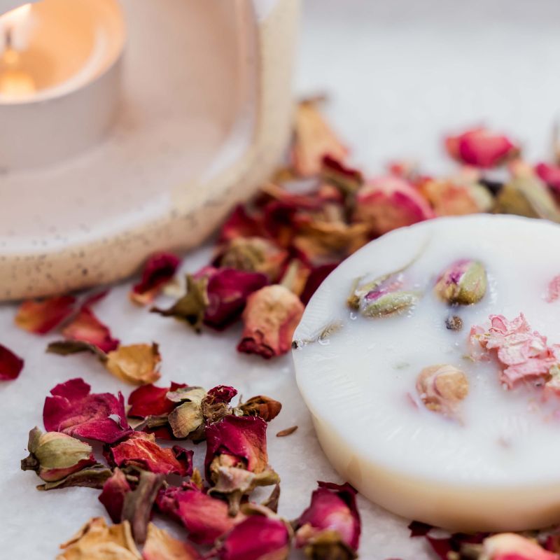 White soap with dried flowers on a white surface with a candle in the background