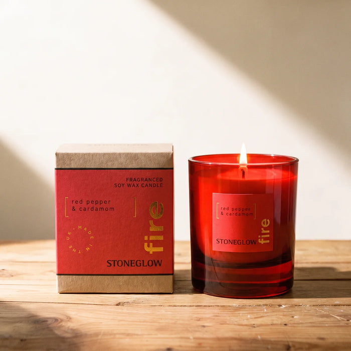Lit Stoneglow candle in a red glass tumbler beside its red and kraft gift box on a sunlit pine table, Fabulous Flowers South Africa